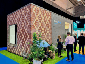 External view of the module in situ at the exhibition. The exterior features a combination of brick slip and grey panel cladding, finished in a diamond pattern.