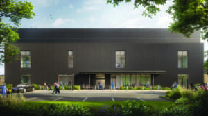 Architectural render of the external design of the new day case unit. The building is finished with ribbed, dark grey cladding and there are large windows on both floors. The main entrance features a large glass area and a wide canopy. A number of people can be seen inside and outside the building.