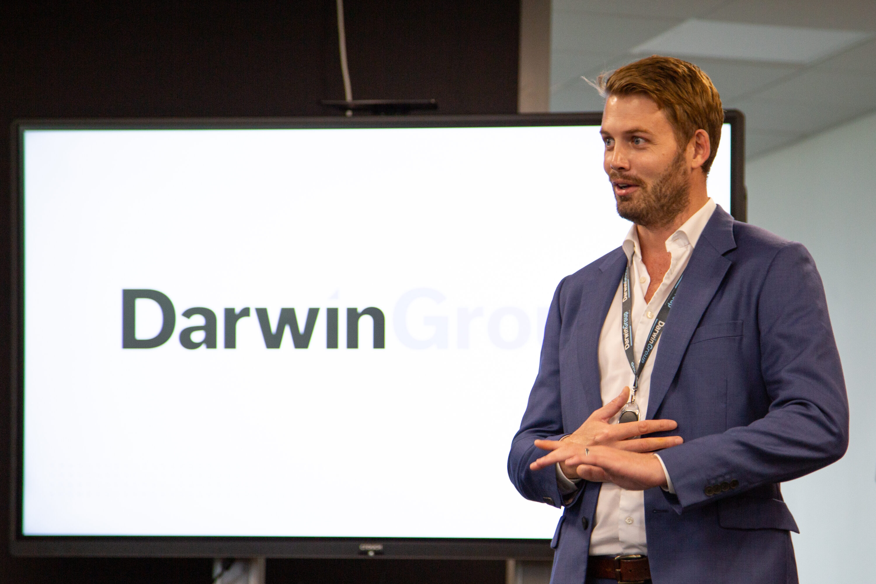 The Darwin Group CEO, Richard Pierce, stood in front of a large display screen, giving a presentation.