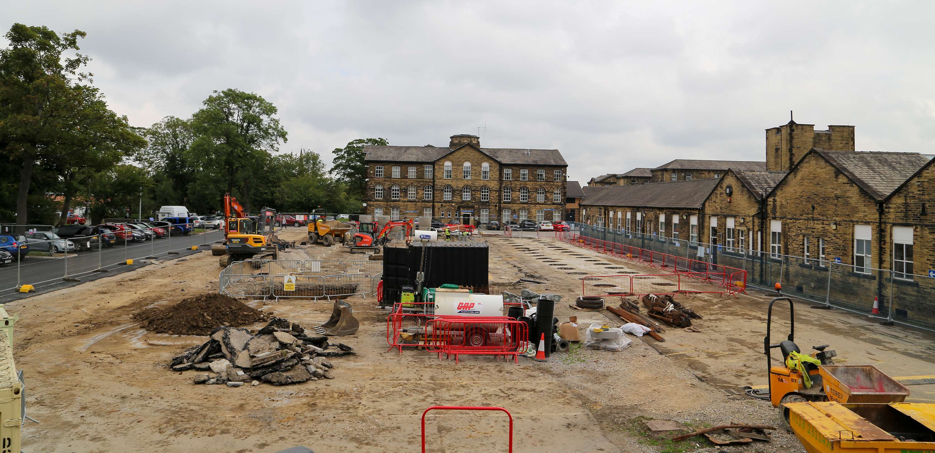 An overview of the St Luke's site in Bradford while groundworks were underway. There is a small site cabin in the middle of the picture, steel fencing all around the construction site and a number of items of plant machinery, including dumper trucks and diggers, around the site.