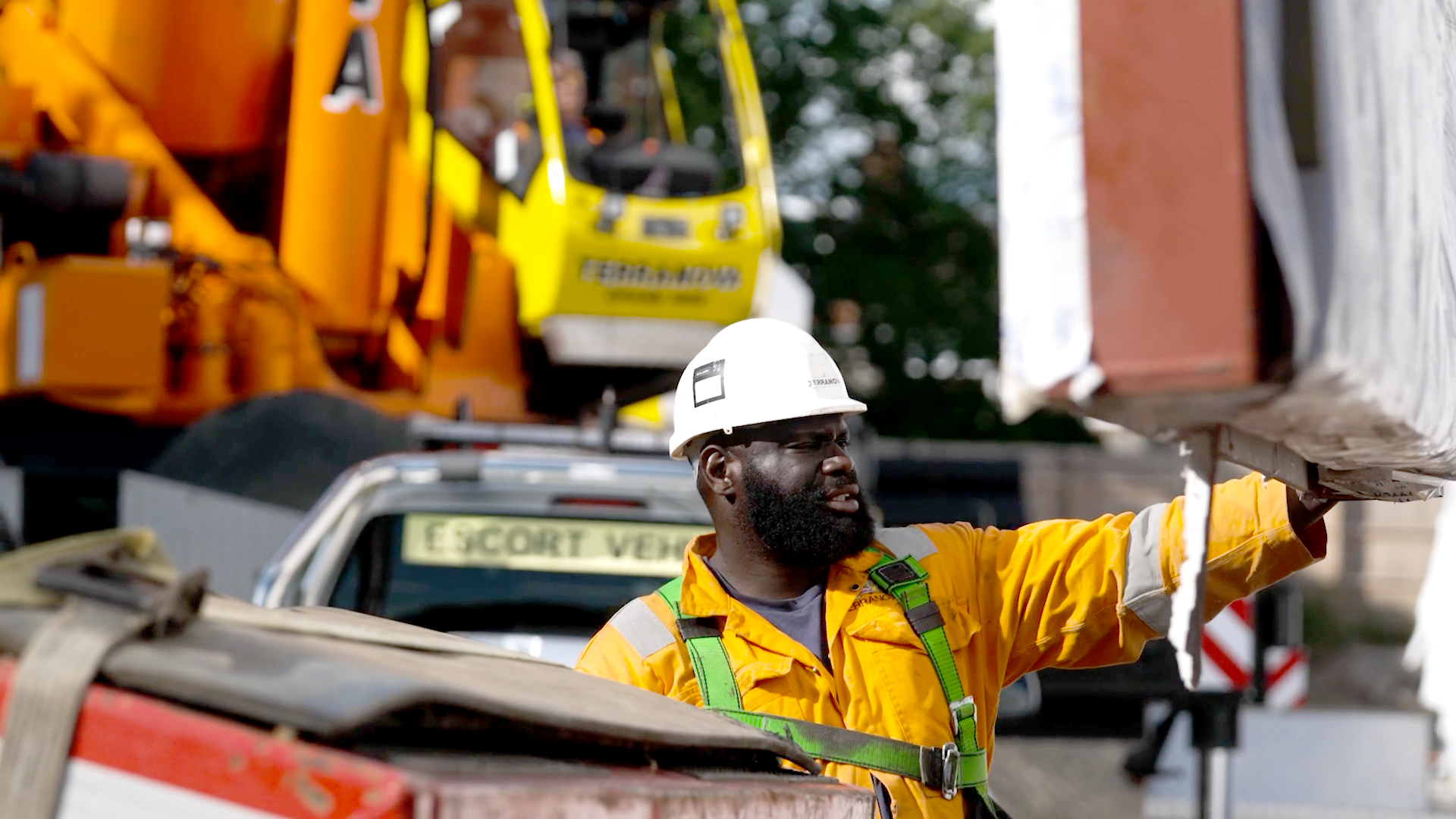 A worker in hard hat and high-vis jacket helps to guide a building module into place. In the background is a crane.