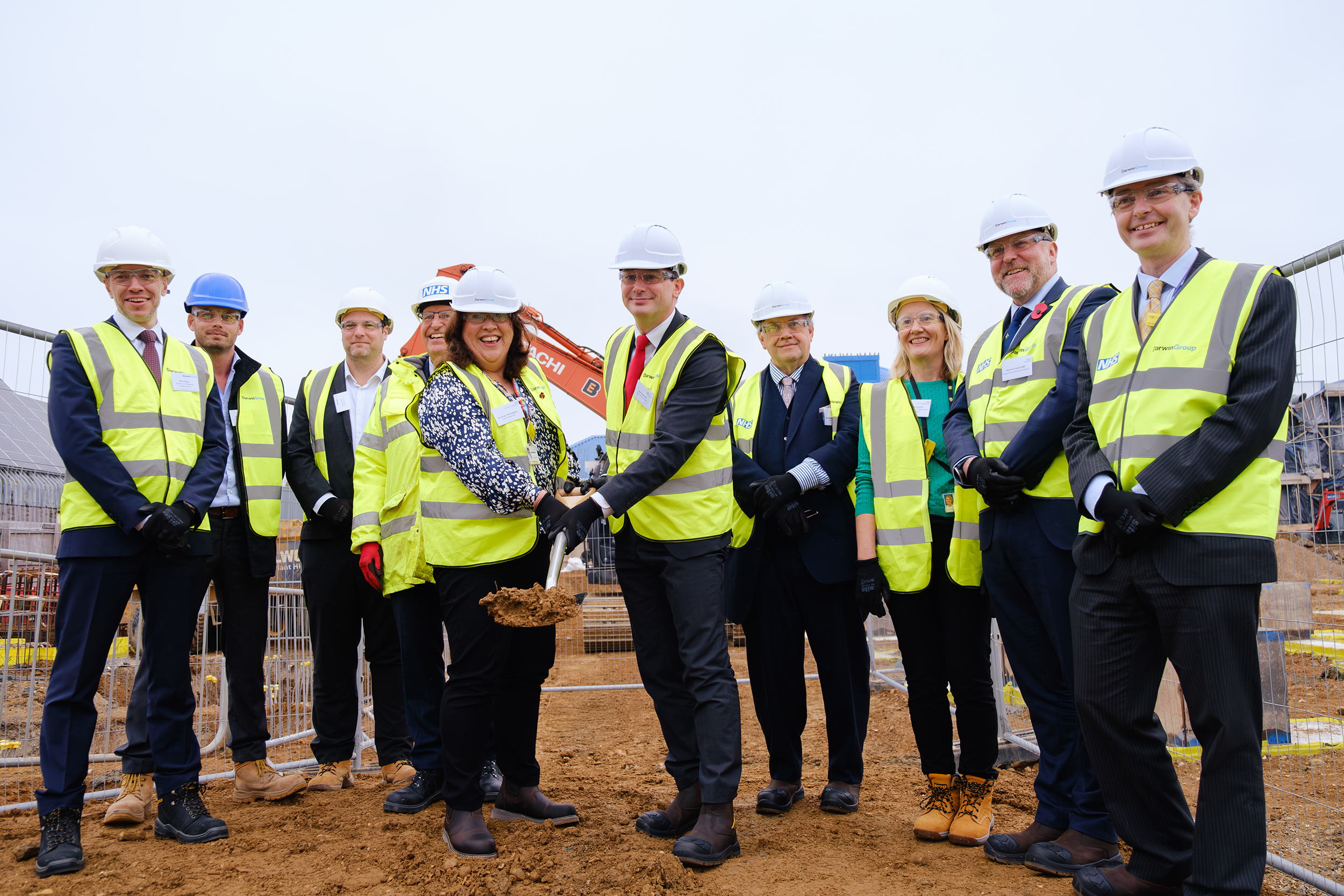 A group of people in PPE at a construction site - the two people at the front are holding a spade full of dirt